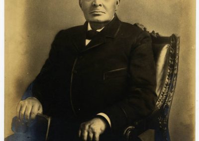 Portrait of Thomas W. Stringer. Image courtesy of Xavier University of Louisiana Library Digital Archives & Collections. Sepia colored photograph. Stringer is seated and looking at the viewer. He has grey hair and is wearing a black suit, black vest, black bowtie, and white shirt.
