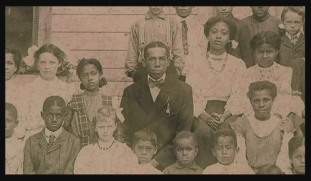 Picture with Black and white students posing in front of Buxton School, 1910