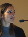 Woman with long brown hair wearing blue turtle neck speaking into mic