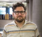 Man with short curly hair and glasses wearing striped shirt